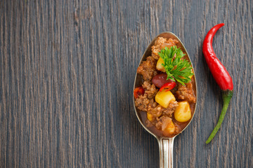 Mexican dish chili con carne in a spoon on a wooden background