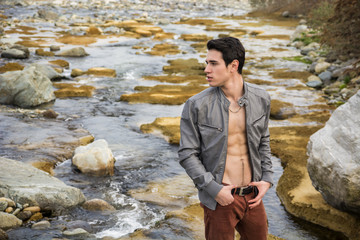 Young man next to river with open jacket on naked torso