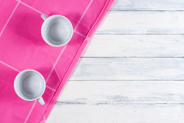 Two coffee cups on pink dishtowel and white wood background