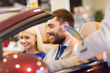 happy couple with car dealer in auto show or salon