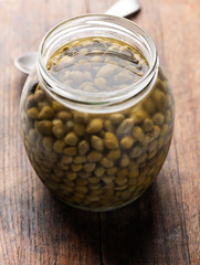 capers in glass jar on wooden background closeup