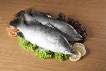 Fresh fish surrounded by lettuce ,lemon and tomatoo