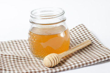 Glass can of honey with a wooden honey dipper on white backgroun