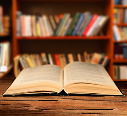 Open book on table on bookshelves background