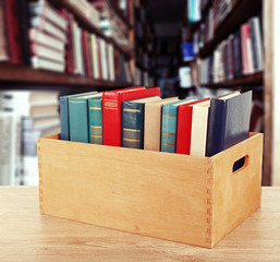 Books in wooden crate on bookshelves background