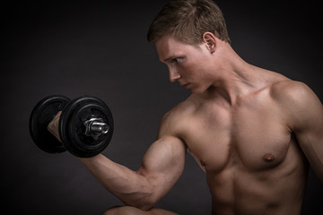 Fototapeta na wymiar Muscular young man doing exercise with dumbbells