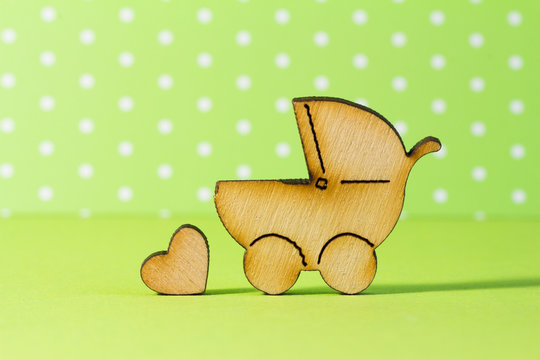 Wooden icon of baby carriage and little heart on green backgroun