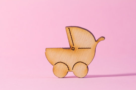 Wooden icon of baby carriage on pink background