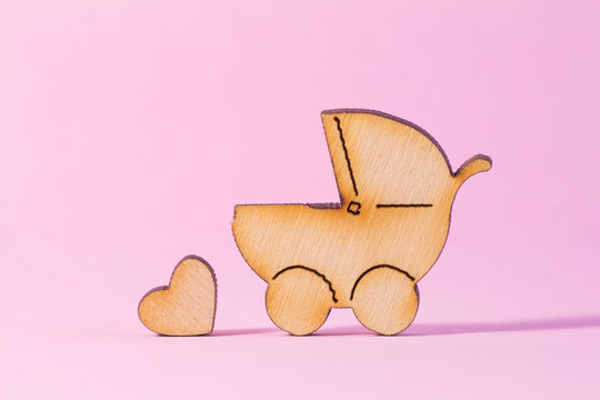 Wooden icon of baby carriage and little heart on pink background