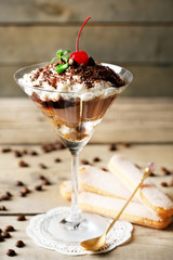 Tasty tiramisu dessert in glass, on wooden background