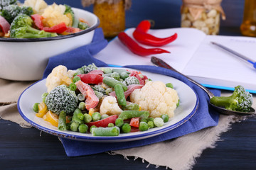 Frozen vegetables on plate on napkin, on wooden table