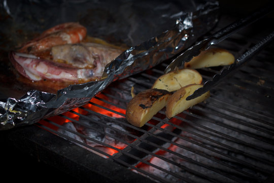 Night scene of cooking potato and seafood in foil on grill