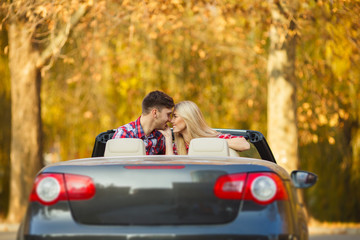Loving couple in a black convertible in the autumn park.