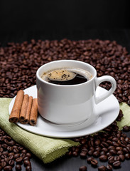 Coffee cup and saucer and coffee beans. Dark background.