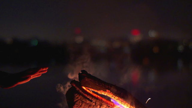The hands by the bonfire. By city and lake background