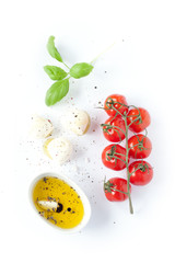 Cherry tomatoes, mozzarella cheese, basil and olive oil on white background from above. Italian caprese salad recipe ingredients.