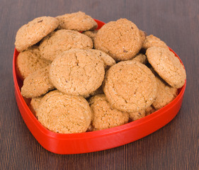 Oatmeal cookies in a red heart plate on a brown surface
