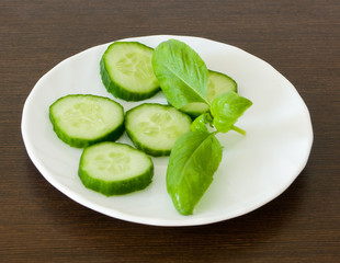 Slices of fresh cucumber with basil leafes on a white plate