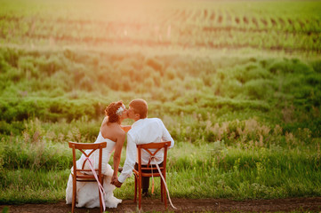 Beautiful young bride and groom kissing sitting on chairs