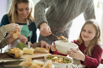 Four people sitting and standing at a table, a man serving food into a bowl.