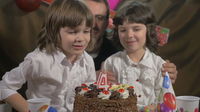 Girl blowing candles on a birthday cake with her father and sist