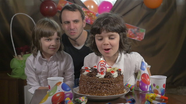 Girl blowing candles on a birthday cake with her father and sist