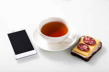 White smartphone,  a cup of tea and sandwich on white glass tabl