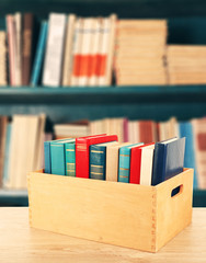 Books in wooden crate on bookshelves background