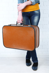 Woman holding old suitcase on brick wall background