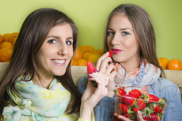 Two beautiful young girls eating strawberries from punnet