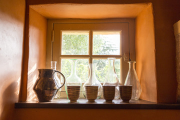 Small window with bottles, jug and cups in an old stone house, o