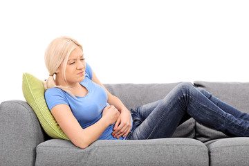 Blond woman feeling stomach pain seated on a gray sofa