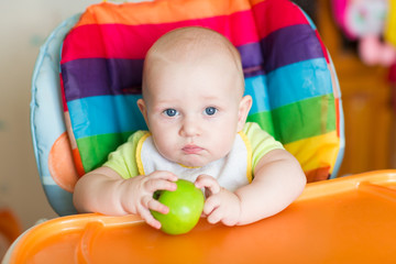 Fototapeta na wymiar Adorable baby eating apple in high chair