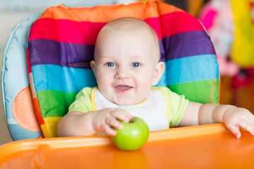 Fototapeta na wymiar Adorable baby eating apple in high chair