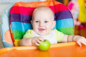 Adorable baby eating apple in high chair