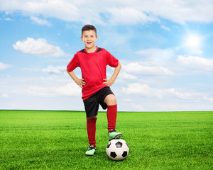 Cheerful youngster standing over a football on field