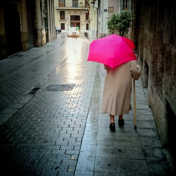 Anciana con paraguas caminando con bast&oacute;n