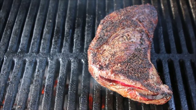 Tri-tip steak cooking on grill with flare ups
