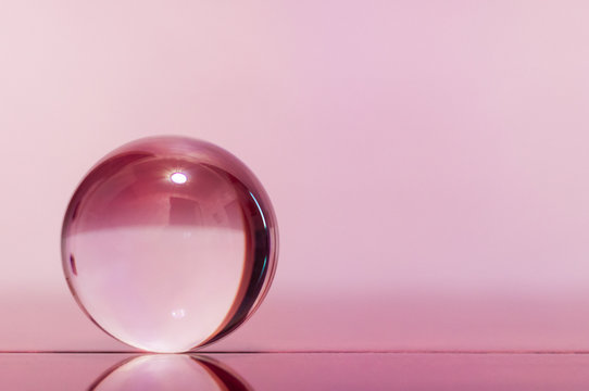 Glass transparent ball on light pink background and mirror