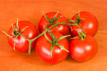 a bunch of large ripe red tomatoes connected by a green branch lying on a red table zoom on full frame