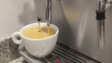 Pouring a coffee espresso on a machine in a white mug