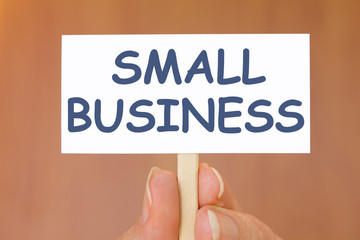 Hand Holding Small Business Sign on Brown Background