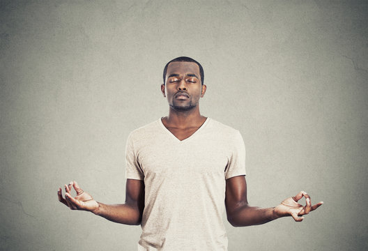 Young man meditating eyes closed on gray wall background 
