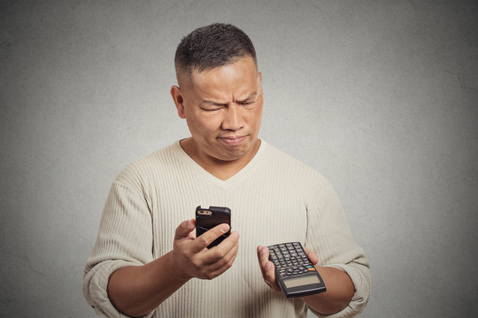 Confused man looking at his smart phone holding calculator