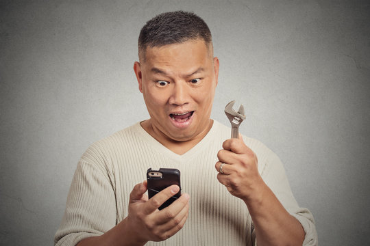 Excited man looking at smartphone holding wrench key instrument