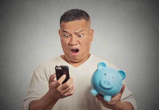 Shocked man looking at his smart phone holding piggy bank