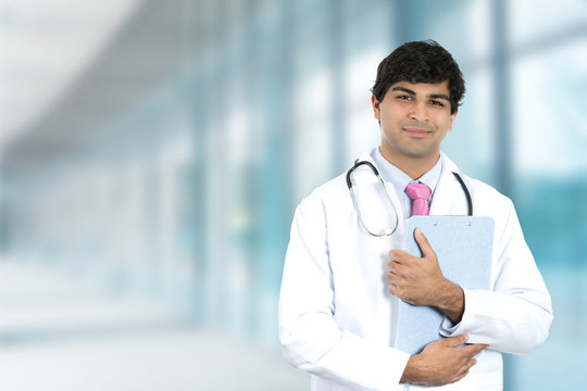 Smiling male doctor with clipboard standing in hospital hallway