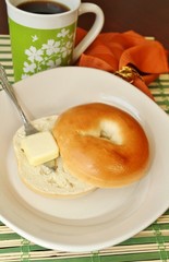 A bagel  with butter and a cup of coffee