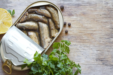Sprats with oil in tin can on wooden board