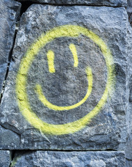 Yellow smiley face painted on surface of stone wall